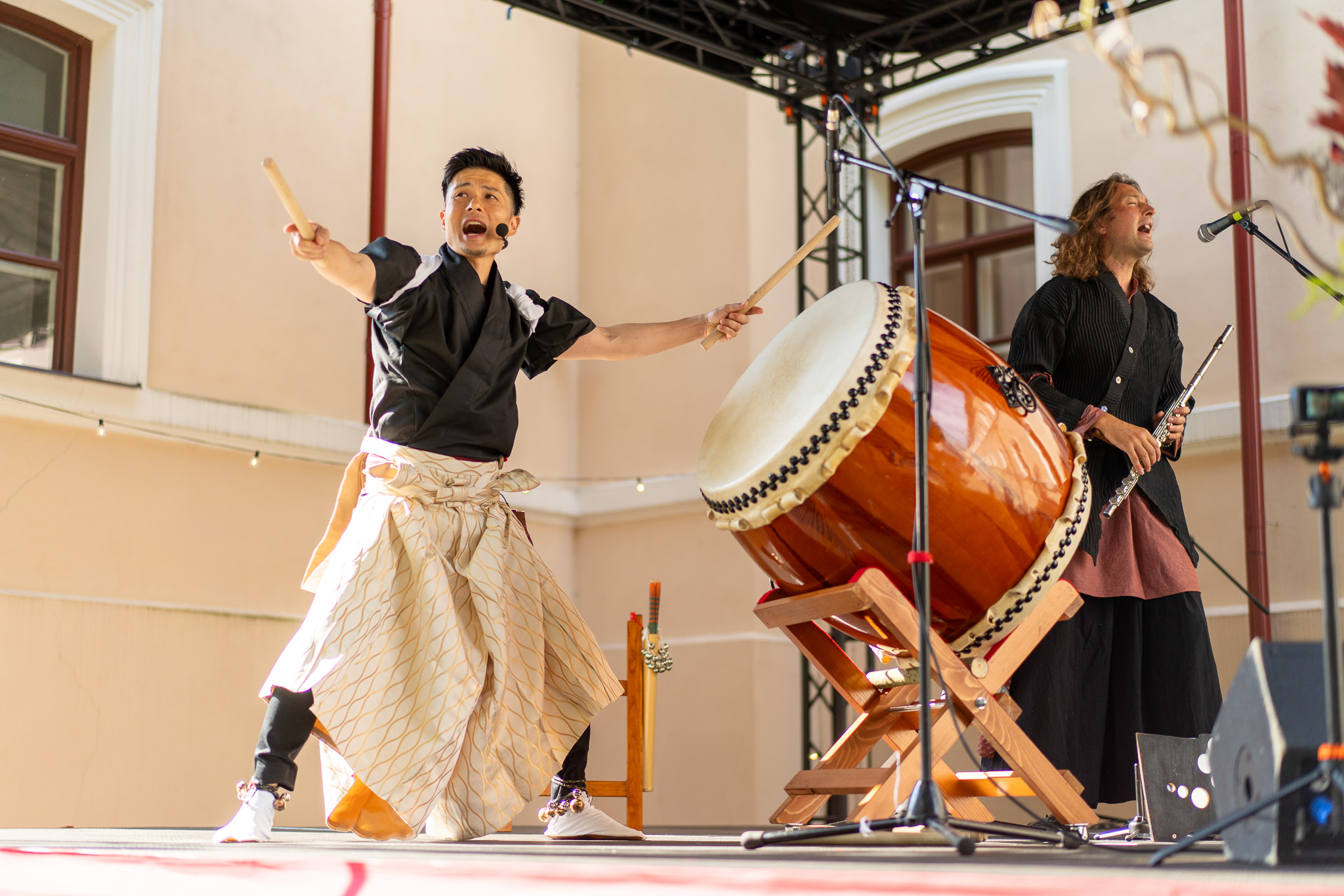 Aki and Mikey dressed in Japanese costumes sing and play drums on stage